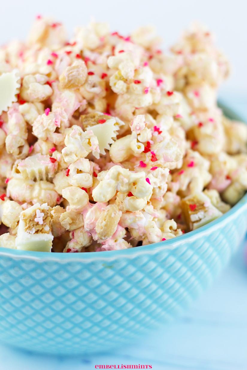 This White Chocolate Peanut Butter Popcorn is a perfect Valentine's Day treat! A blend of white chocolate, peanut butter, peanuts, and Reese's White Chocolate Peanut Butter Cups! Find the recipes on www.Embellishmints.com