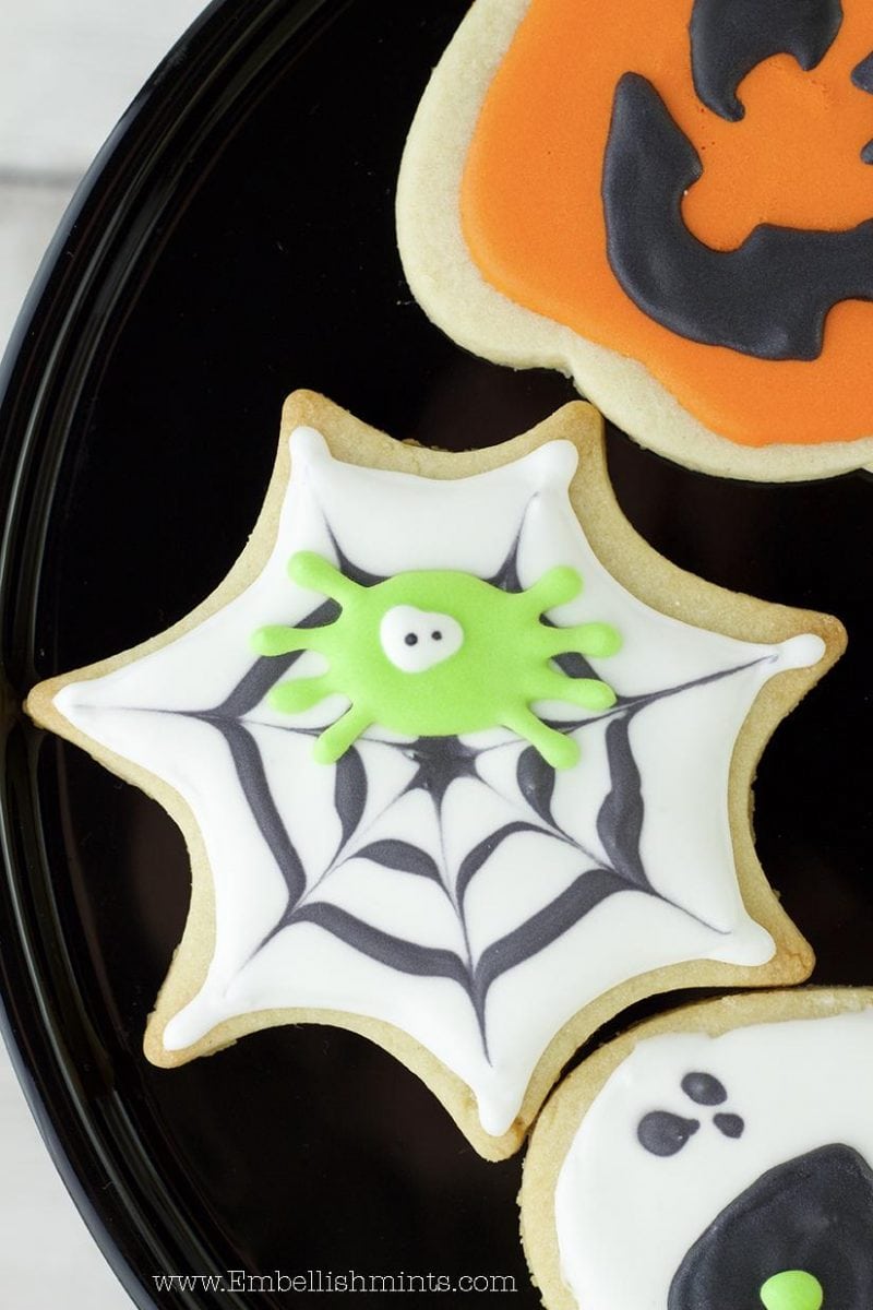 Watch how I made these super fun Halloween Spiderweb Cookies using Royal Icing. Get inspired for Halloween with these Spiderweb Cookies. www.Embellishmints.com